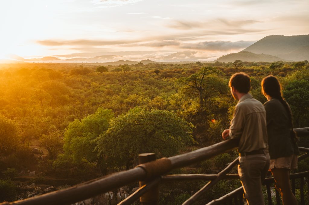 Beautiful sunset shot. Two people lean on a railing overlooking rolling African landscapes